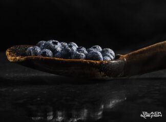 Du kan va blåbär i slev, fotokonst av Garip Jensen för Black & Design. Vattenpärlor på blåbär i en gammal träslev fotad på nära håll i en mörk miljö.